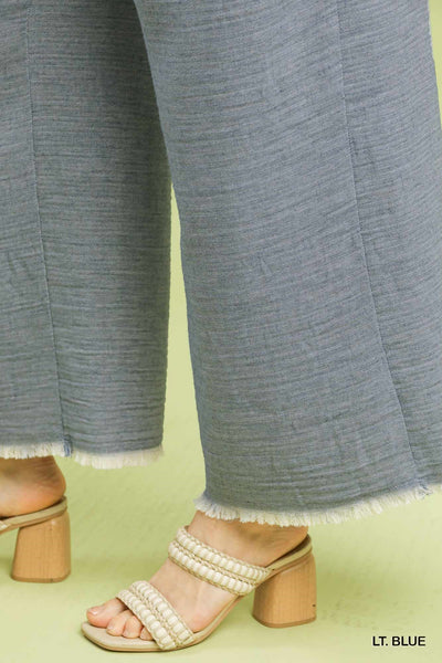 Light blue pants with frayed hem and beige sandals on a light green background