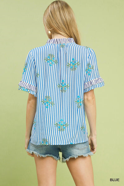 Woman wearing a blue and white striped shirt with floral additions on a green background