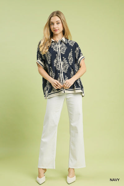 Woman wearing a navy patterned shirt and white pants on a light green background