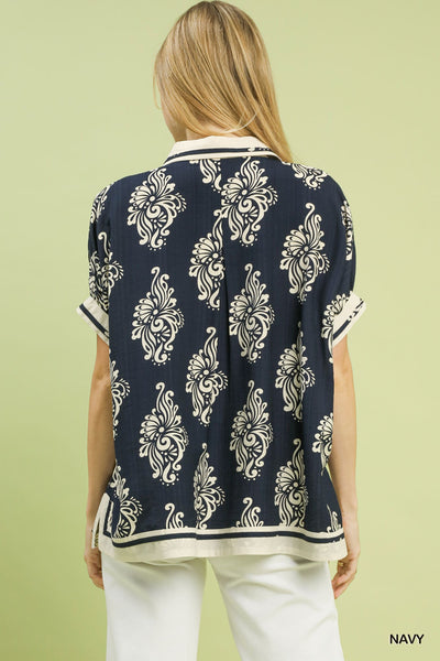 Woman wearing a navy blue patterned top with white pants on a light green background