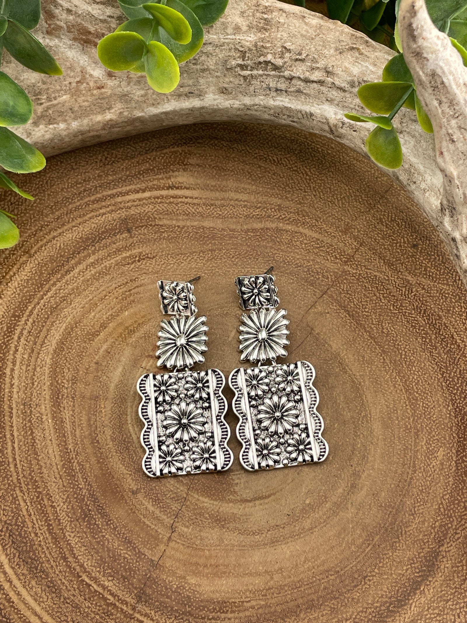 Silver floral earrings on a wooden surface with green leaves.