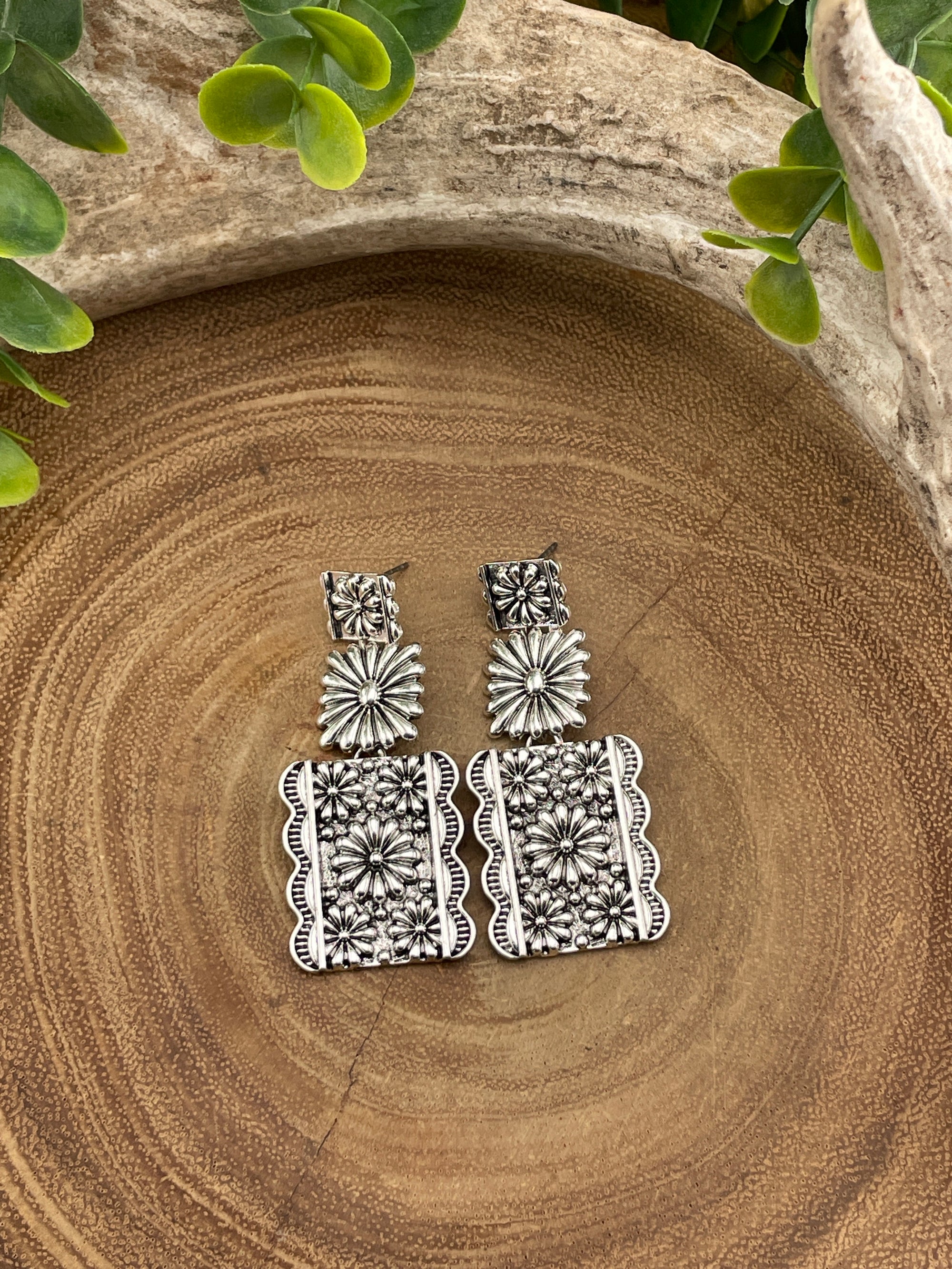 Silver floral earrings on a wooden surface with green leaves.