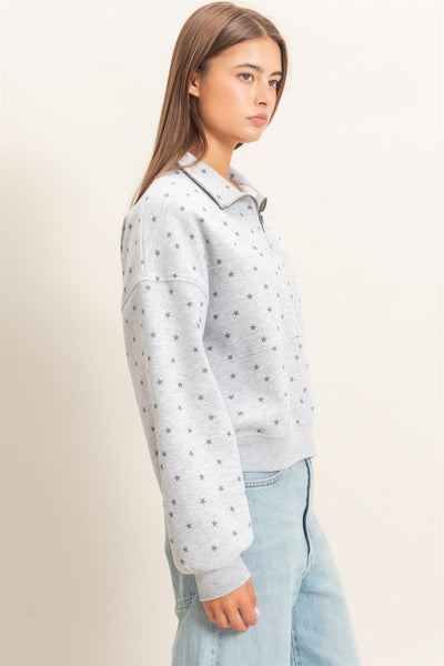 side view of model wearing gray half zip sweatshirt with stars and jeans before a light background