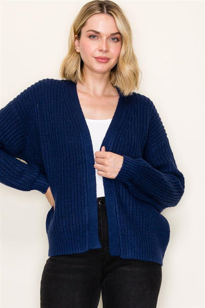 Woman wearing a blue cardigan over a white top against a plain background