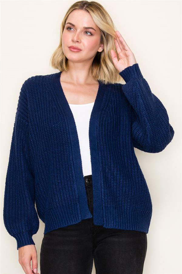 Woman wearing a blue cardigan over a white top and black pants on a light background