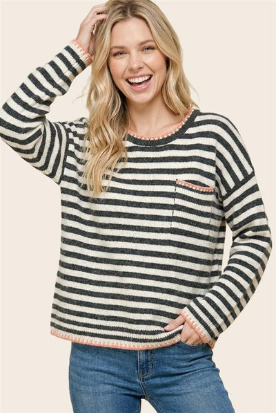 model wearing a cream sweatshirt with gray striped and pink accents and blue jeans.