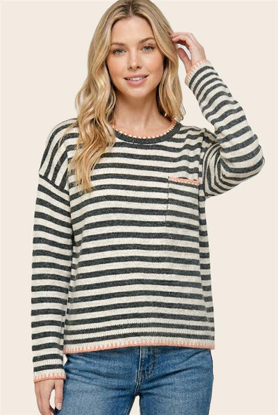 model wearing a cream sweatshirt with gray striped and pink accents and blue jeans.