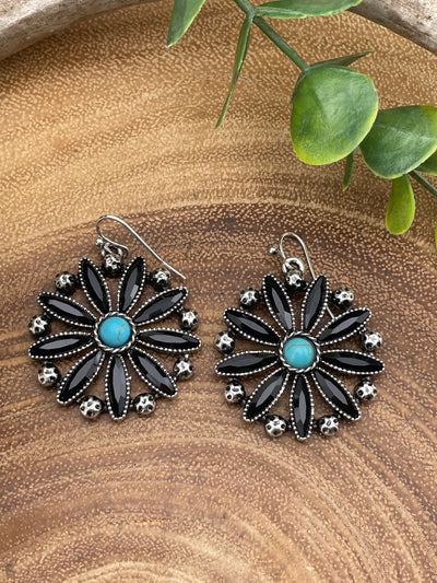 Pair of floral earrings with turquoise centers on a wooden surface.