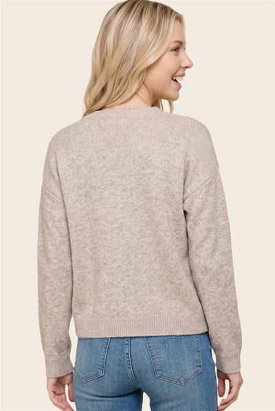 A woman shown from the back wearing a light beige knit sweater and blue jeans against a plain cream background.