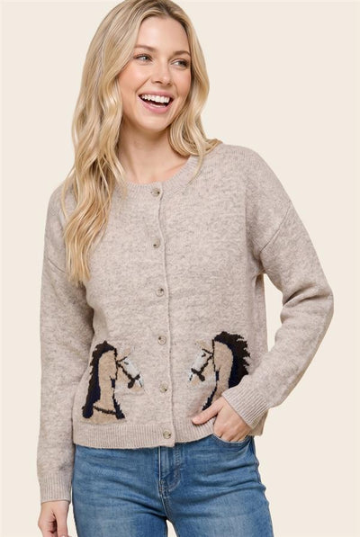 A woman wearing a light beige button-up cardigan sweater with embroidered horse designs on the lower front, paired with blue jeans, against a solid light beige background.
