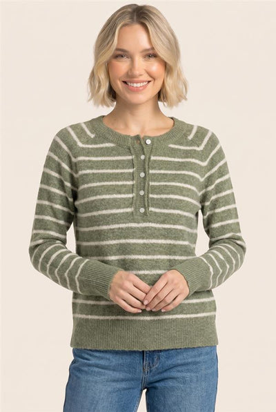 A woman wearing a green and cream striped knit henley sweater with blue jeans, standing against a solid light beige background.