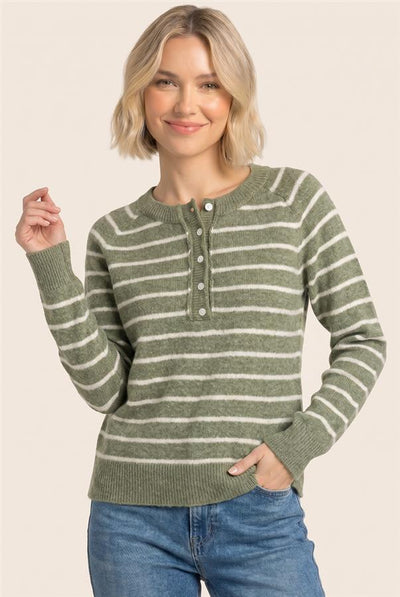 A woman wearing a green and white horizontally striped knit henley sweater with blue jeans, standing against a solid light beige background.
