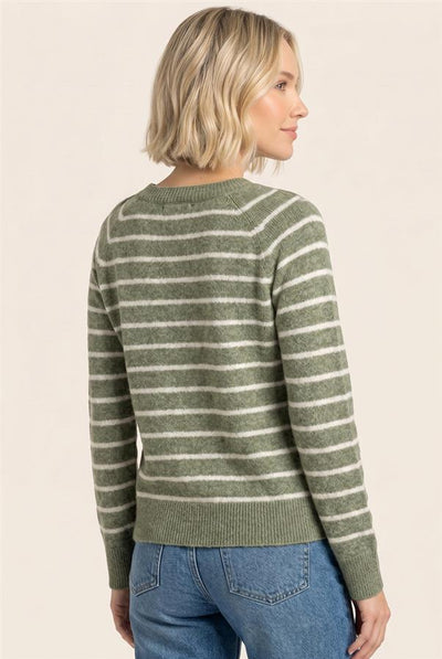 A woman with short blonde hair is shown from the back wearing a sage green and white striped knit sweater with blue jeans, set against a plain beige studio background.
