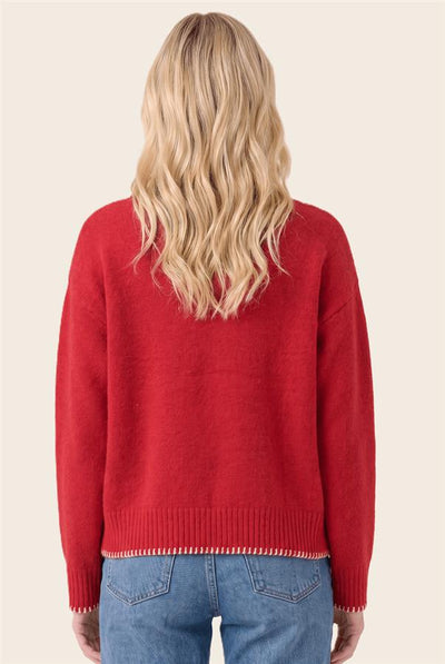 A woman viewed from behind wearing a bright red knit sweater and blue jeans against a plain light beige studio background.