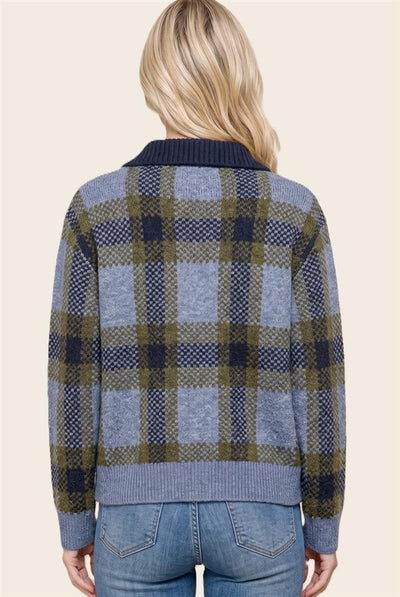 A woman viewed from the back wearing a blue, olive green, and navy plaid knit cardigan sweater with blue jeans, set against a solid light beige background.