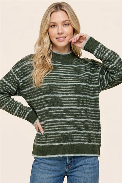 A woman wearing a dark green and gray striped knit sweater with blue jeans, posing against a solid beige background.