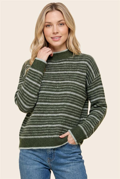 A woman modeling a green and white striped knit sweater with blue jeans against a solid beige background.