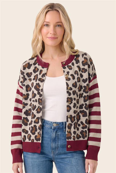 A woman modeling a leopard print and striped cardigan with burgundy ribbed trim, worn over a white tank top and blue jeans against a light beige background.