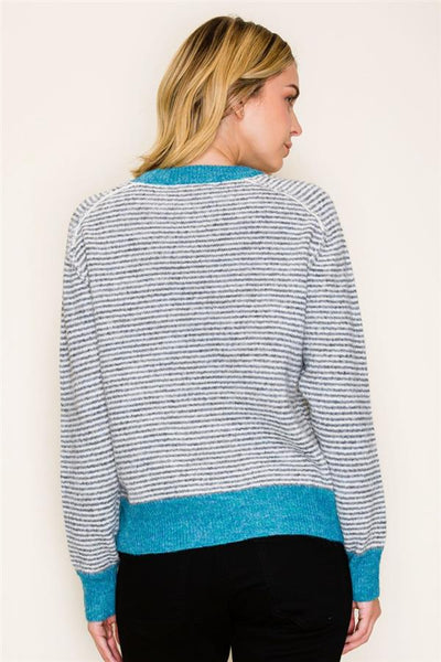 A woman shown from the back wearing a heathered gray and white striped sweater with bright turquoise blue ribbed trim at the collar, cuffs, and hem, paired with black pants against a plain off-white background.