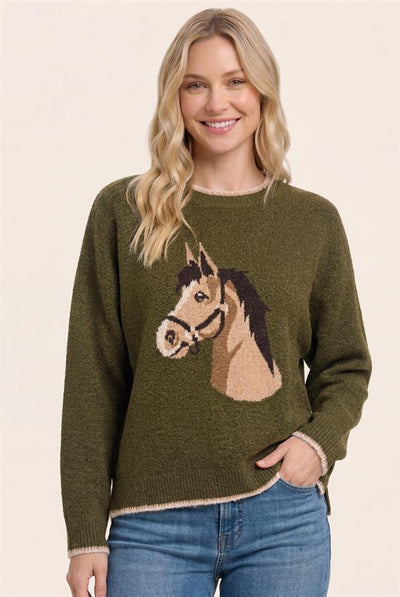 A woman wearing an olive green knit sweater with a large horse head motif on the front, paired with blue jeans, against a plain beige background.