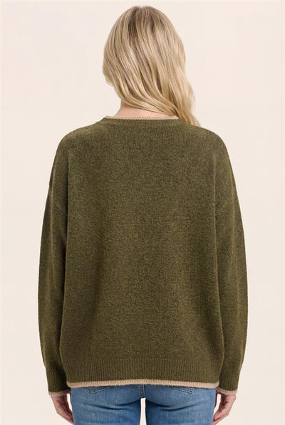A woman viewed from the back wearing an oversized olive green knit sweater and blue jeans against a plain light beige studio background.
