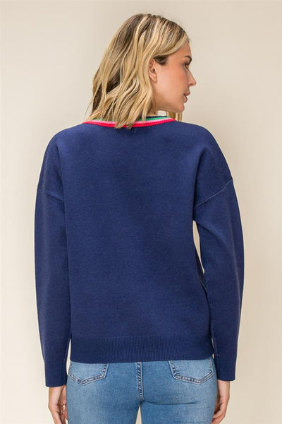 A woman shown from the back wearing a navy blue knit sweater with a thin red and green striped collar trim, paired with light blue jeans, against a plain beige background.