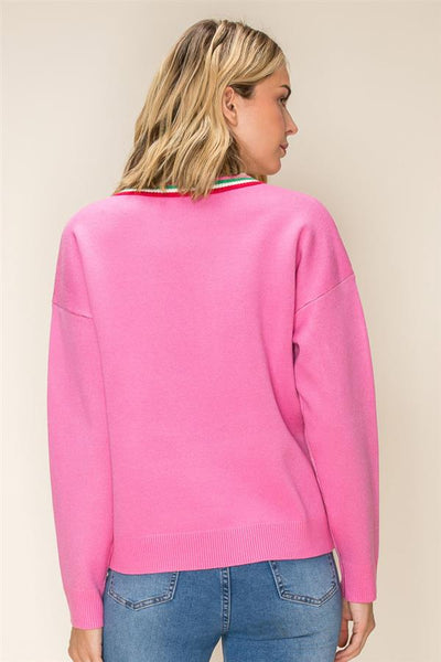 A woman shown from the back wearing a bright pink knit sweater with a thin multicolor striped collar trim, paired with blue jeans, against a plain beige background.