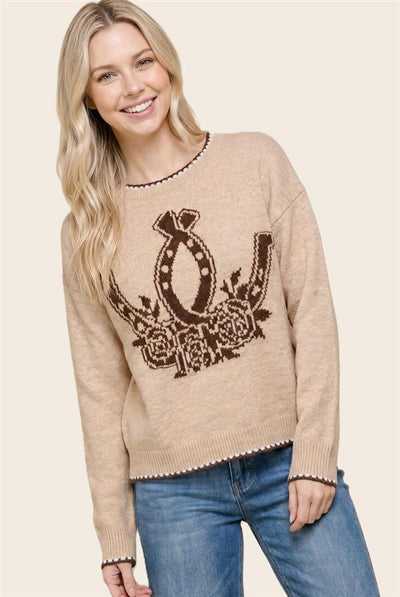 model wearing a taupe sweater with horseshoes and flowers and blue jeans