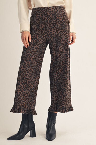 model wearing an ivory blouse, leopard pants with a ruffle hem & black boots with a beige background