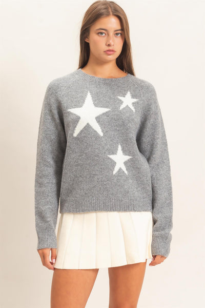model wearing gray sweater with white stars and a white skirt on a light background