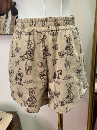 Beige shorts with a dark brown cowboy and cactus pattern, displayed on a white dress form mannequin.