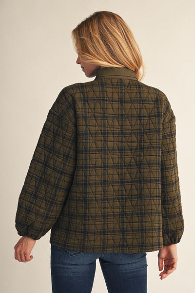 A woman shown from the back wearing a quilted plaid jacket in olive green and black, paired with blue jeans, against a plain beige studio background.