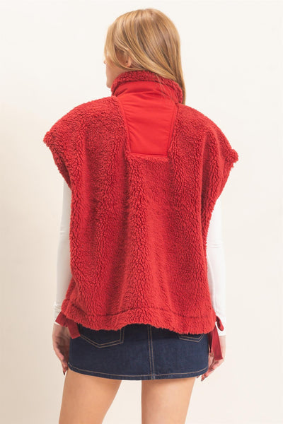 back of a model wearing white shirt and jeans skirt with a red Sherpa Vest over it.