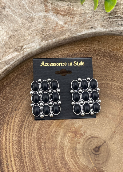 Pair of black and silver earrings on a 'Accessorize in Style' card against a wooden background