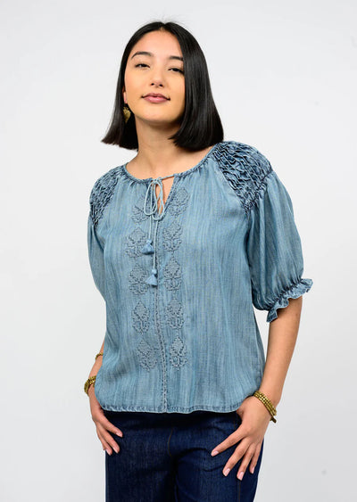 Woman wearing a blue embroidered blouse against a white background