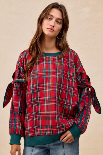 Woman wearing a red plaid sweater with tied sleeves on a beige background