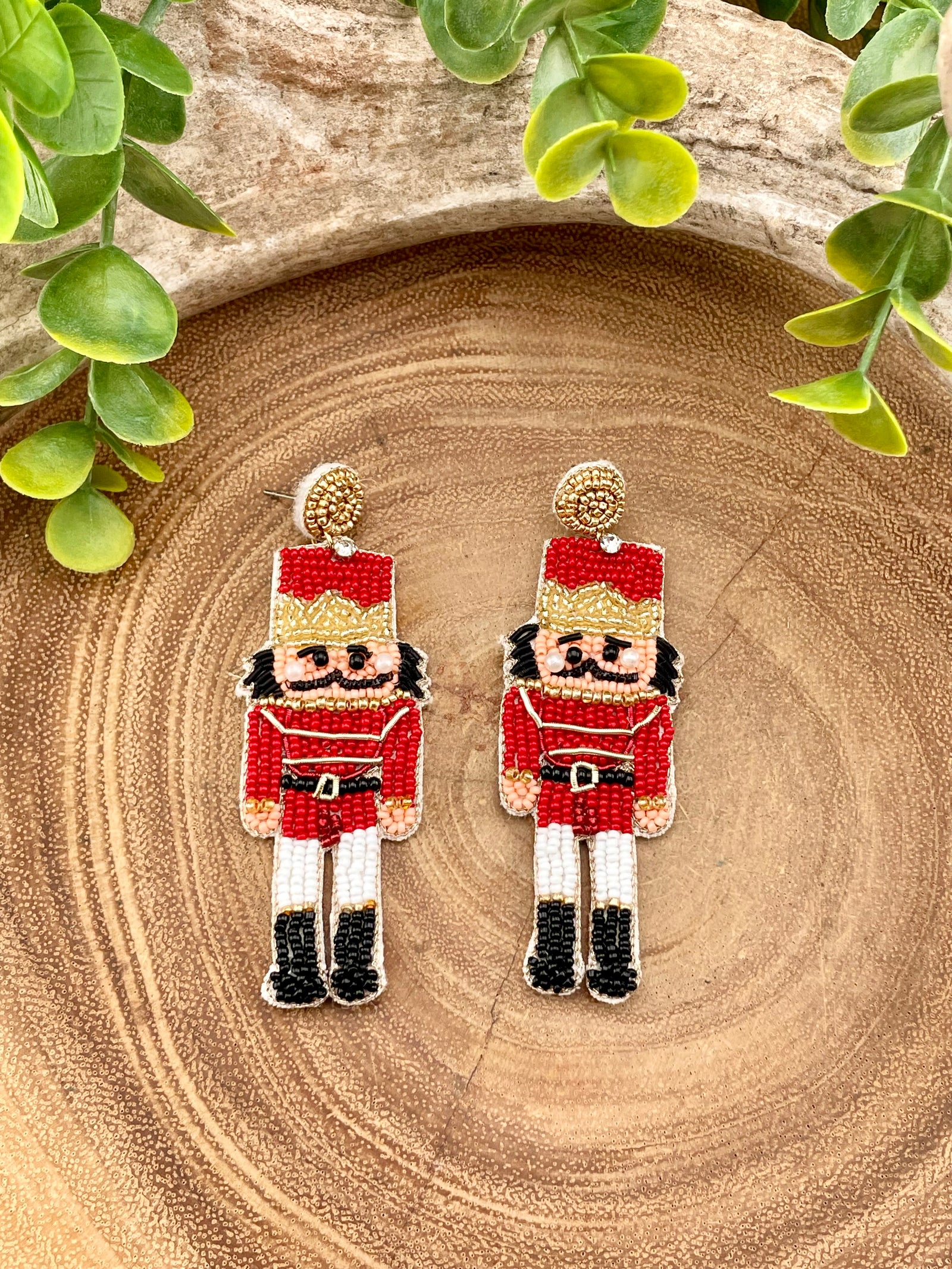 Nutcracker-themed earrings on a wooden surface with green leaves.