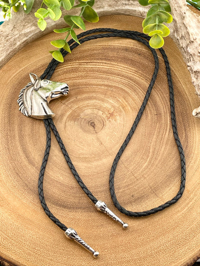 Bolo tie with horse head design on a wooden surface