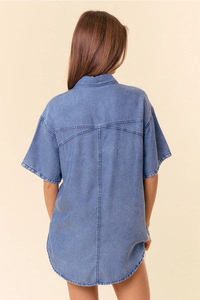 back of model wearing a short sleeve denim top & white shorts with a tan background