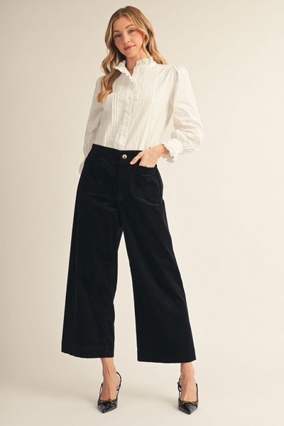 model wearing a white blouse, black heels and black corduroy pants on a beige background