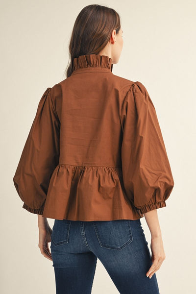 A woman shown from the back wearing a brown puff-sleeve blouse with a ruffled high neck and gathered peplum hem, paired with blue jeans, against a plain beige studio background.