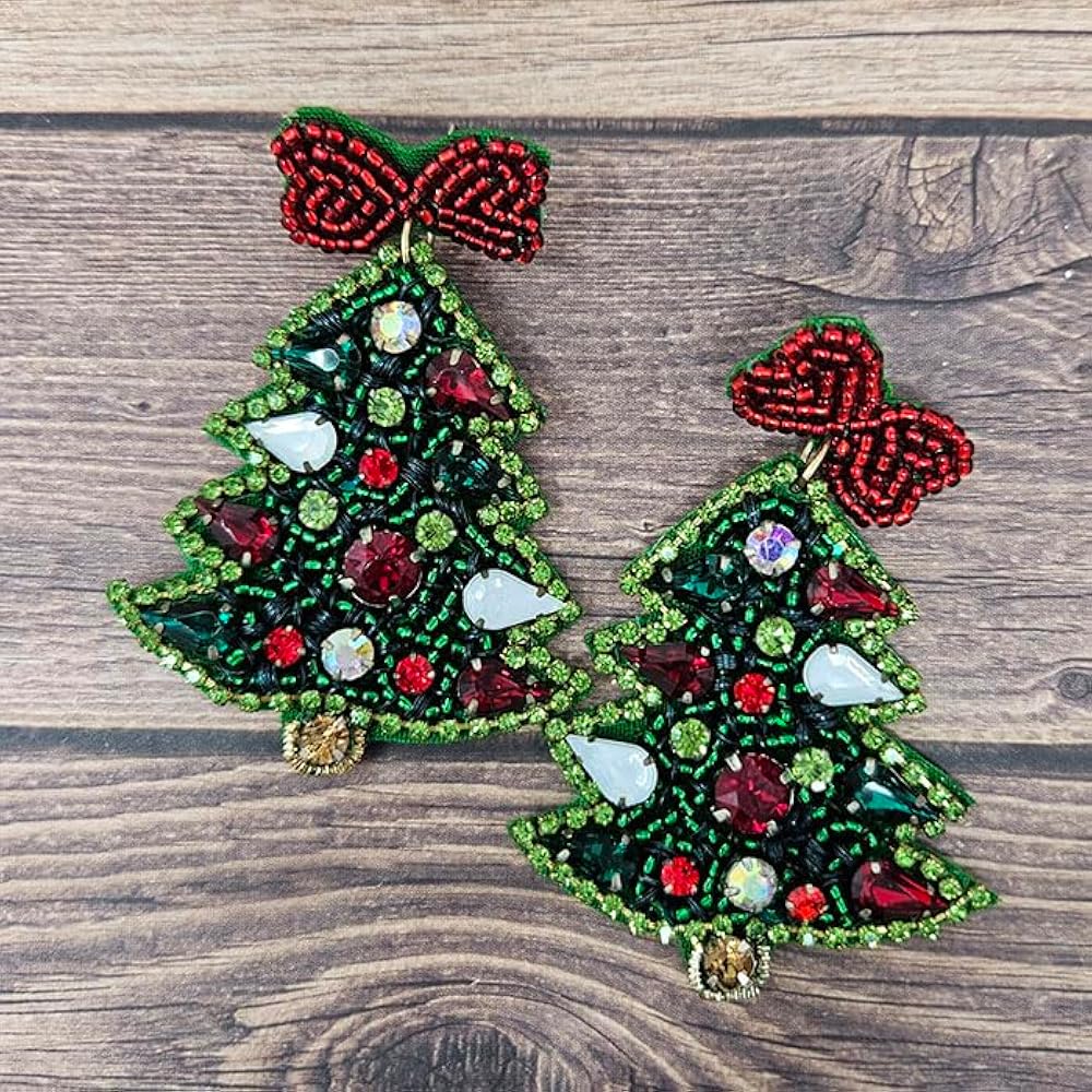 A pair of beaded Christmas tree earrings with red bows and green accents placed on a wooden surface.