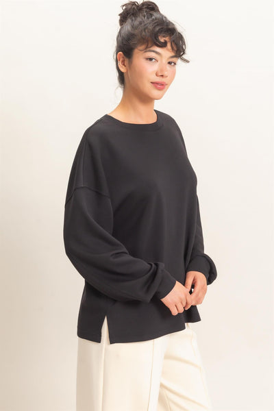 model wearing oversized black sweatshirt with white pants before a light background