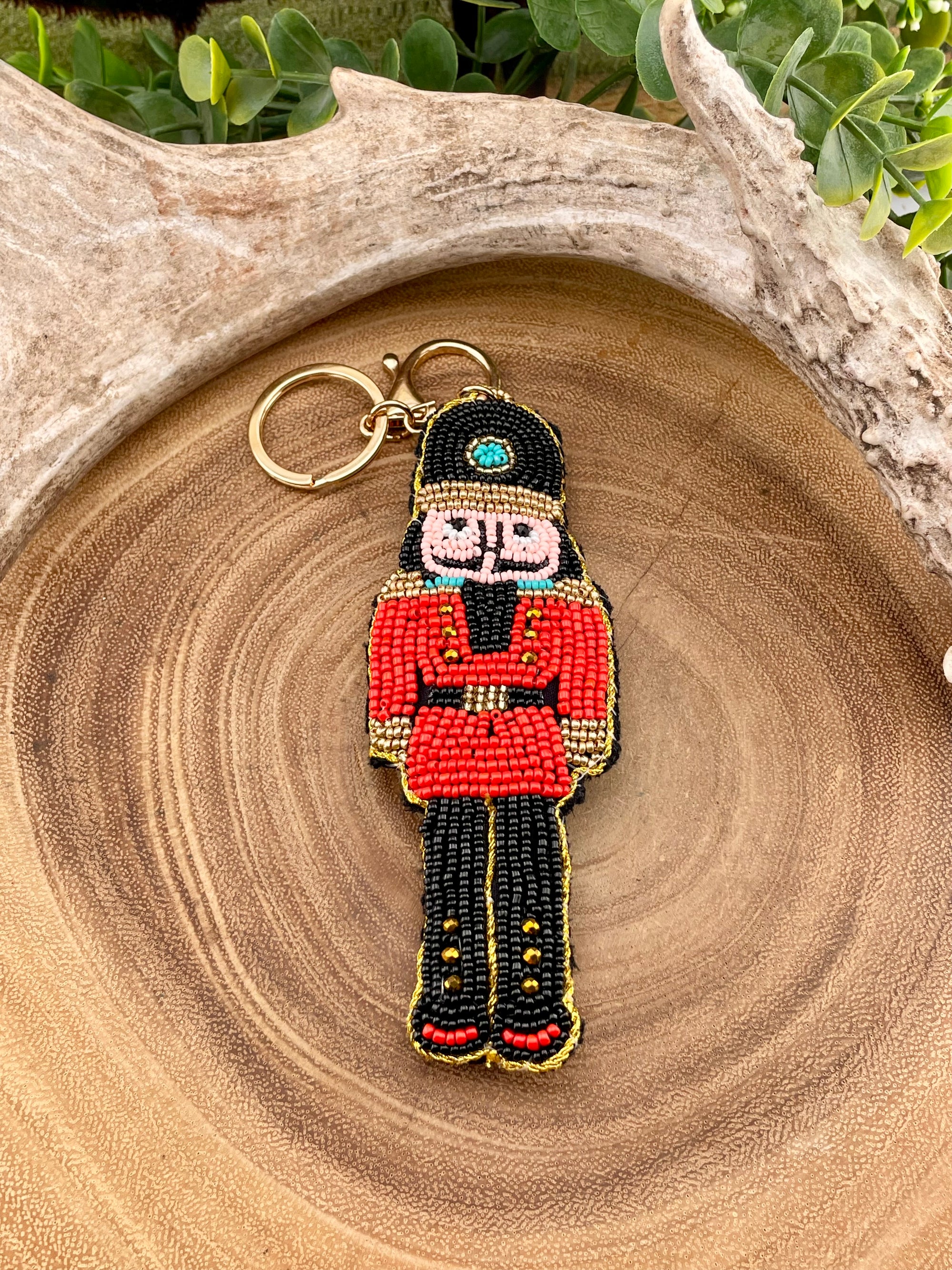 Decorative keychain shaped like a nutcracker on a wooden surface with greenery in the background