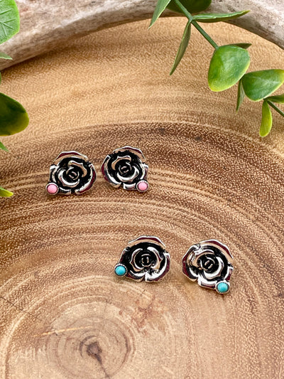 Rose-shaped earrings with pink or turquoise stones on a wooden surface.