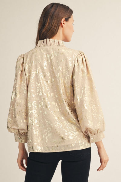 Back of woman wearing a beige metallic blouse with black pants on a plain background