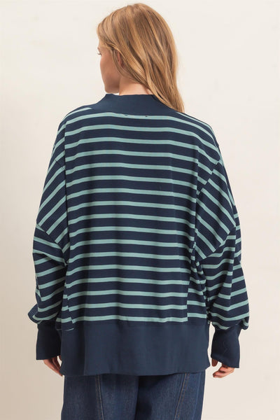 back of woman wearing a navy/sage striped sweatshirt and jeans with a light background