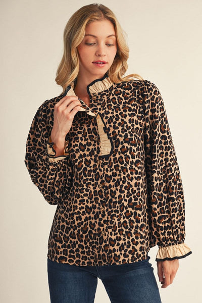A woman wearing a leopard-print long-sleeve blouse with beige ruffled trim on the collar, placket, cuffs, and hem, paired with blue jeans, against a solid light beige background.