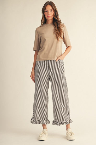 Woman wearing a beige top and striped pants on a plain background