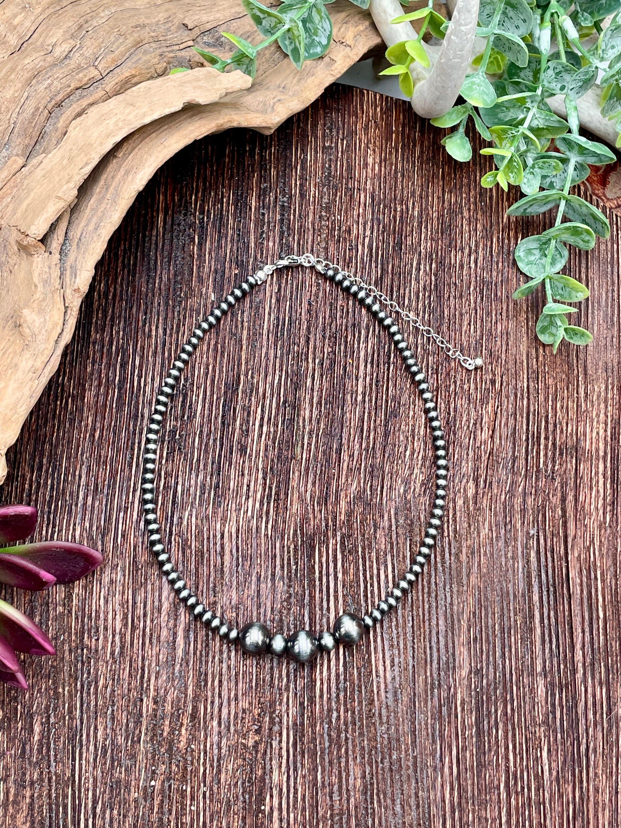 Necklace with silver beads on a wooden surface with greenery